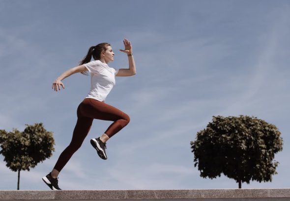 Athletic woman running on an outdoor road, demonstrating fitness and determination under a blue sky.